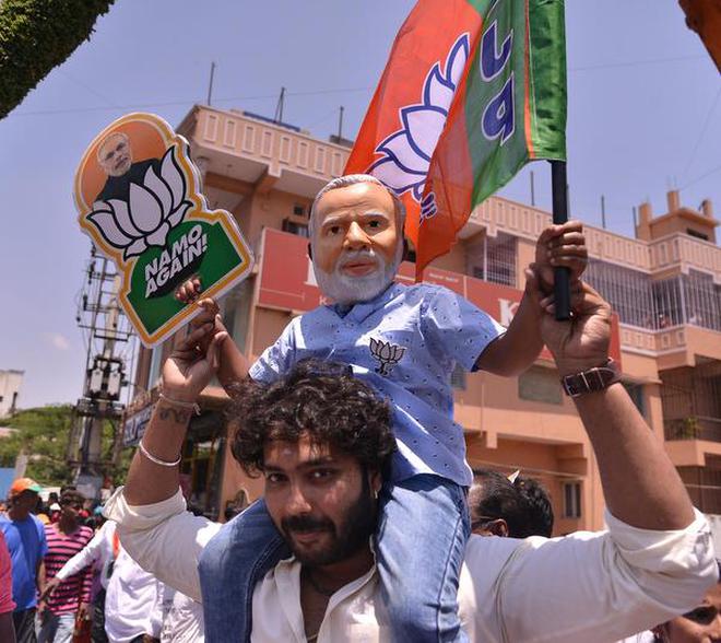A BJP worker carries a boy wearing a Modi mask at a rally in Bengaluru on Tuesday.