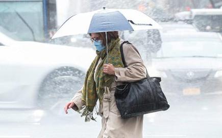 A woman wearing a facemask crosses the street in the rain on March 28, 2020 in New York City.