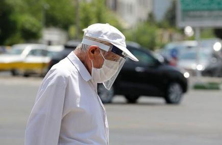 A pedestrian wearing a protective mask and a shield due to coronavirus pandemic walks along a street in Tehran on June 28, 2020.