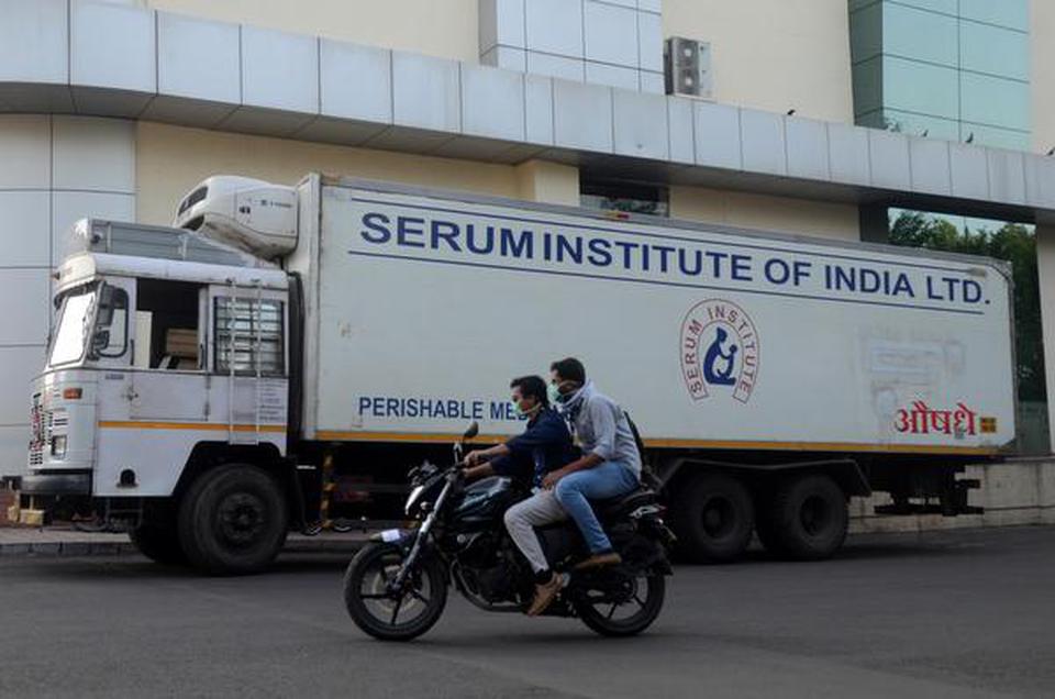 Men ride on a motorbike past a supply truck of Serum Institute in Pune on May 18, 2020.